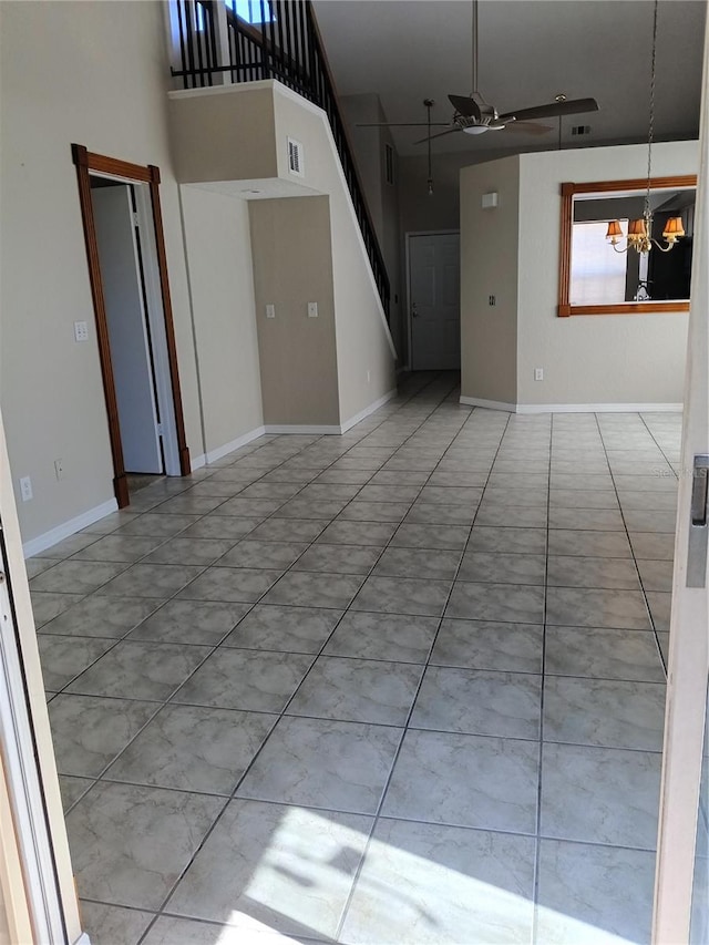 tiled empty room featuring ceiling fan with notable chandelier and a high ceiling