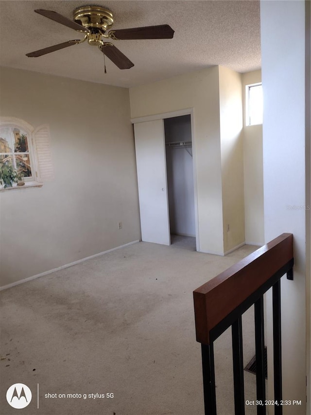 unfurnished bedroom featuring ceiling fan, a closet, a textured ceiling, and carpet flooring