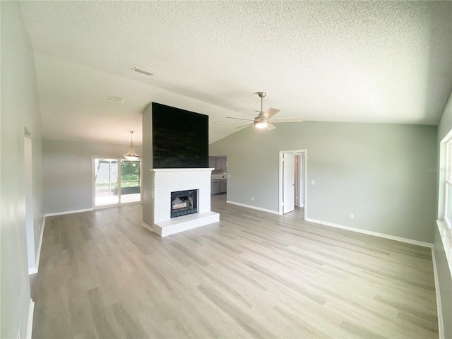 unfurnished living room with a brick fireplace, light hardwood / wood-style floors, lofted ceiling, ceiling fan, and a textured ceiling