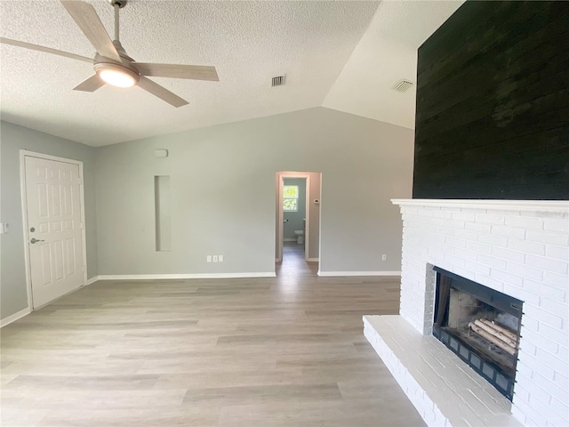 unfurnished living room with light wood-type flooring, a fireplace, a textured ceiling, ceiling fan, and lofted ceiling