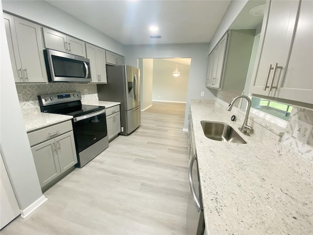 kitchen with light stone countertops, appliances with stainless steel finishes, light hardwood / wood-style floors, sink, and decorative backsplash