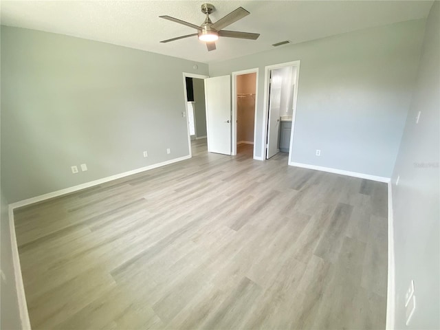 unfurnished bedroom with a walk in closet, a closet, connected bathroom, ceiling fan, and light wood-type flooring