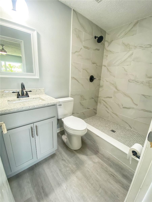 bathroom with hardwood / wood-style flooring, toilet, a tile shower, vanity, and a textured ceiling