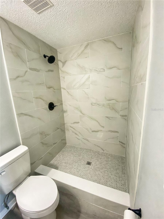 bathroom with toilet, a tile shower, and a textured ceiling