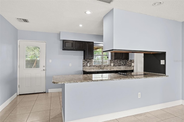 kitchen featuring light stone countertops, kitchen peninsula, a textured ceiling, black electric cooktop, and sink