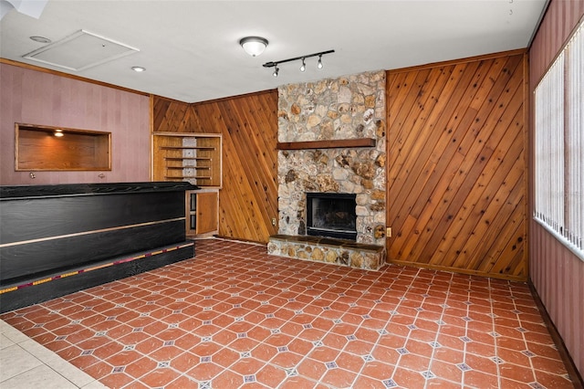 unfurnished living room featuring a fireplace, rail lighting, and wood walls