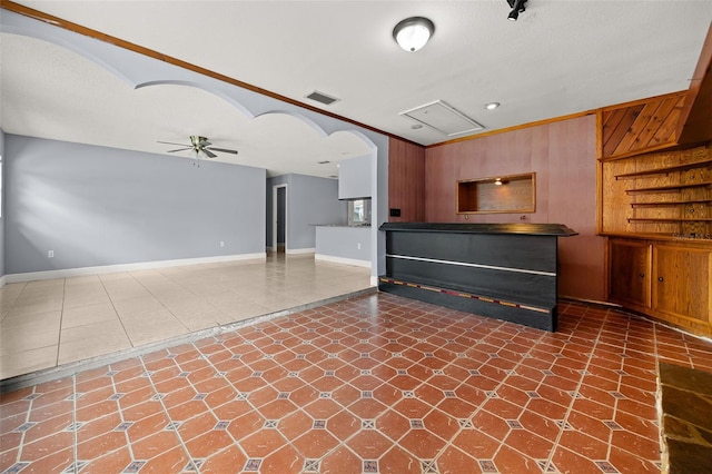 unfurnished living room featuring a textured ceiling, ceiling fan, crown molding, and wood walls