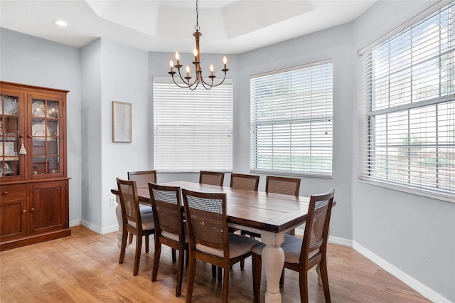 dining area with a notable chandelier, plenty of natural light, light hardwood / wood-style floors, and a raised ceiling