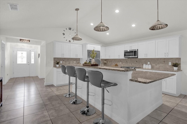 kitchen featuring white cabinetry, a kitchen island with sink, appliances with stainless steel finishes, and vaulted ceiling