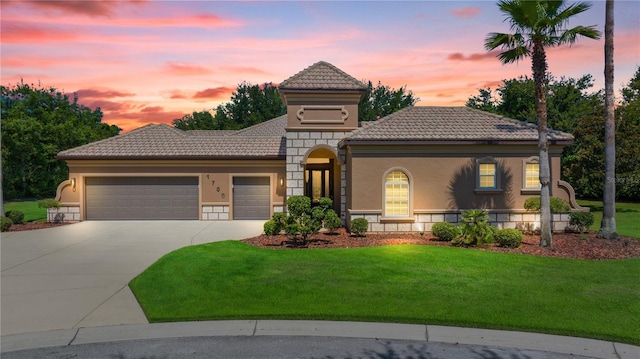 mediterranean / spanish home featuring a garage, a tiled roof, stone siding, stucco siding, and a front lawn