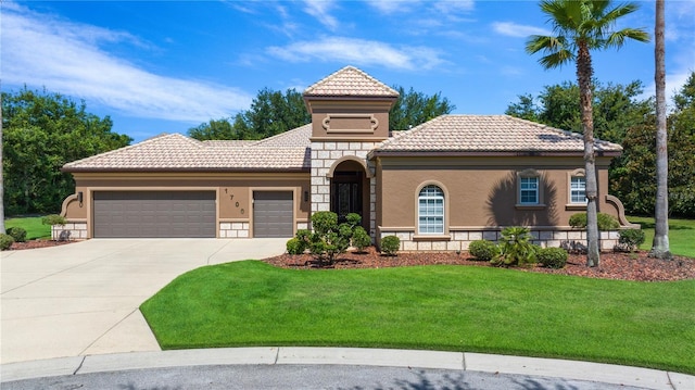 mediterranean / spanish house featuring a tile roof, stucco siding, a front yard, a garage, and stone siding