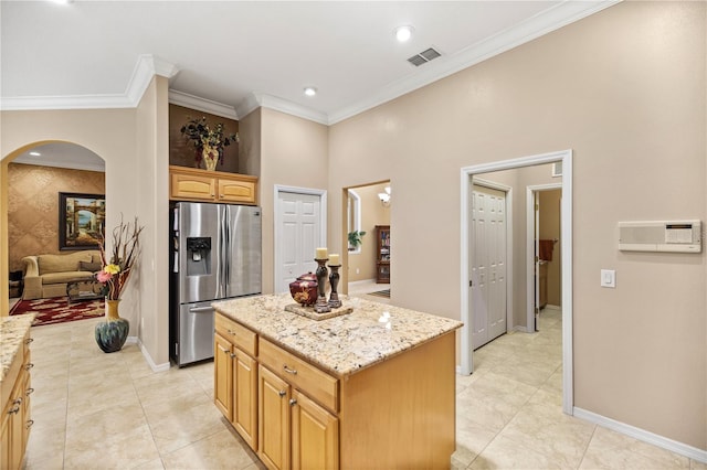 kitchen with light stone countertops, a center island, crown molding, stainless steel fridge, and light tile patterned floors