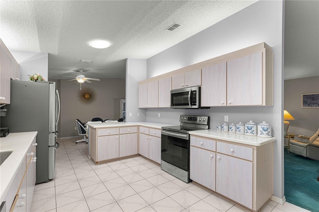 kitchen with stainless steel appliances, light brown cabinets, kitchen peninsula, ceiling fan, and a textured ceiling