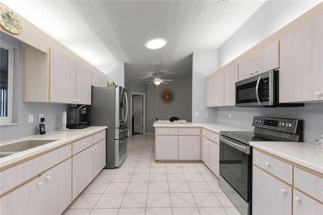 kitchen featuring light brown cabinetry, light tile patterned floors, appliances with stainless steel finishes, ceiling fan, and a textured ceiling