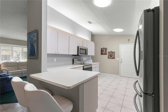 kitchen with light tile patterned floors, a textured ceiling, kitchen peninsula, and stainless steel appliances