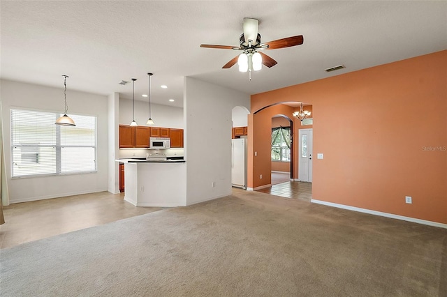 unfurnished living room with ceiling fan with notable chandelier and light carpet