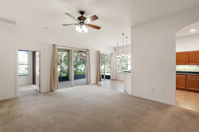 unfurnished living room with a wealth of natural light, ceiling fan, and light colored carpet