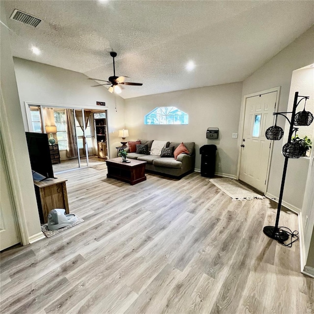 living room with ceiling fan, a textured ceiling, lofted ceiling, and light wood-type flooring