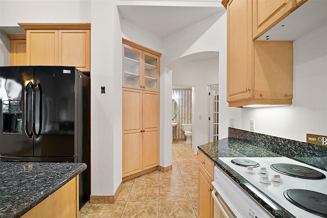 kitchen featuring light brown cabinetry, light tile patterned floors, dark stone counters, and white appliances