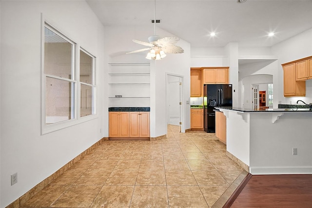 kitchen with built in shelves, ceiling fan, black fridge, kitchen peninsula, and a breakfast bar area