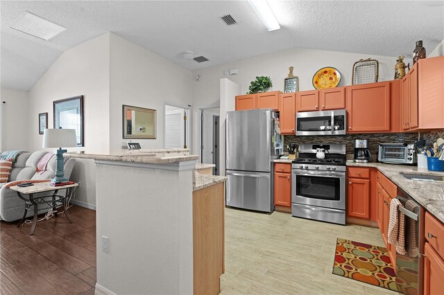 kitchen with light wood-type flooring, appliances with stainless steel finishes, vaulted ceiling, and backsplash