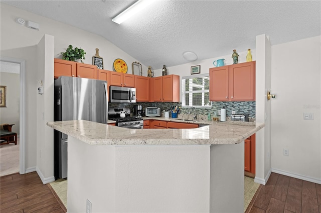 kitchen featuring appliances with stainless steel finishes, vaulted ceiling, sink, and light hardwood / wood-style floors