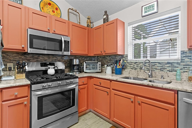 kitchen with a textured ceiling, backsplash, stainless steel appliances, light stone counters, and sink