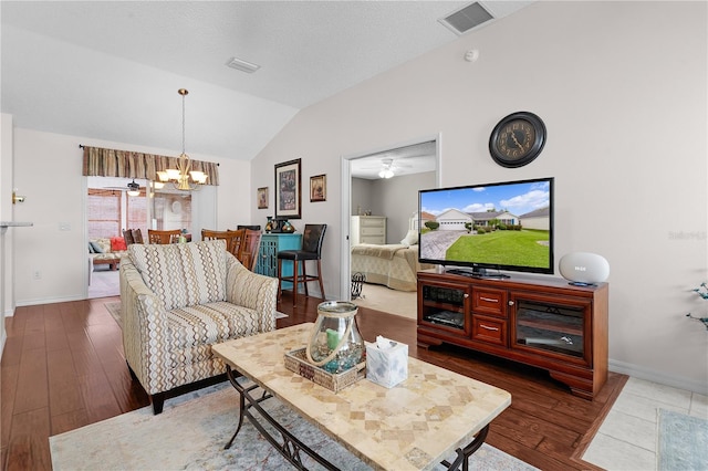 living room with ceiling fan with notable chandelier, vaulted ceiling, a textured ceiling, and light hardwood / wood-style flooring