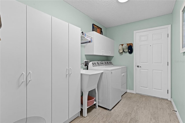 laundry area with a textured ceiling, baseboards, light wood-type flooring, cabinet space, and washing machine and clothes dryer