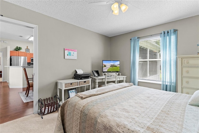 bedroom with a textured ceiling, ceiling fan, light wood-style flooring, and freestanding refrigerator