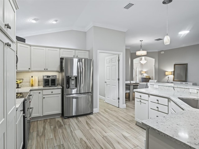 kitchen featuring light stone countertops, backsplash, stainless steel appliances, vaulted ceiling, and decorative light fixtures