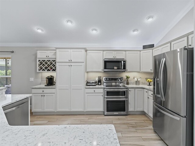 kitchen featuring light stone countertops, appliances with stainless steel finishes, backsplash, vaulted ceiling, and ornamental molding