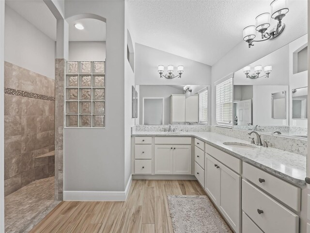 bathroom featuring lofted ceiling, wood-type flooring, vanity, a tile shower, and a textured ceiling