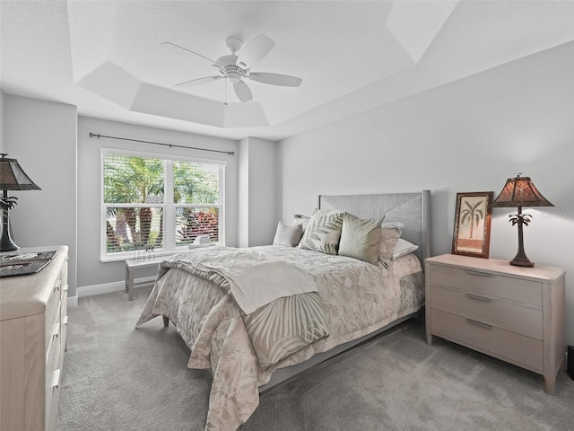 bedroom with a ceiling fan, a raised ceiling, light colored carpet, and baseboards