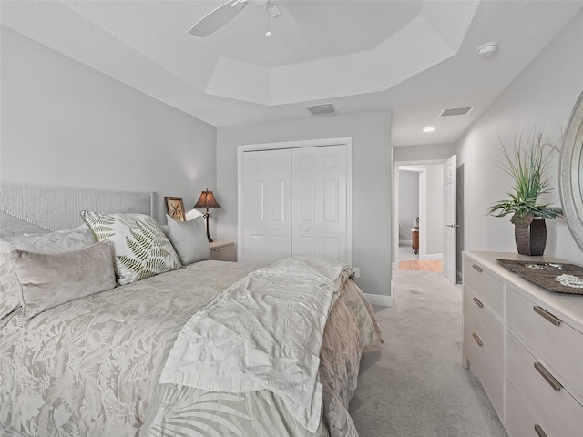 bedroom featuring a closet, ceiling fan, a raised ceiling, and light colored carpet