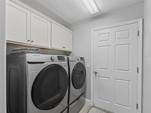 clothes washing area with washer and dryer, a textured ceiling, cabinets, and light hardwood / wood-style floors