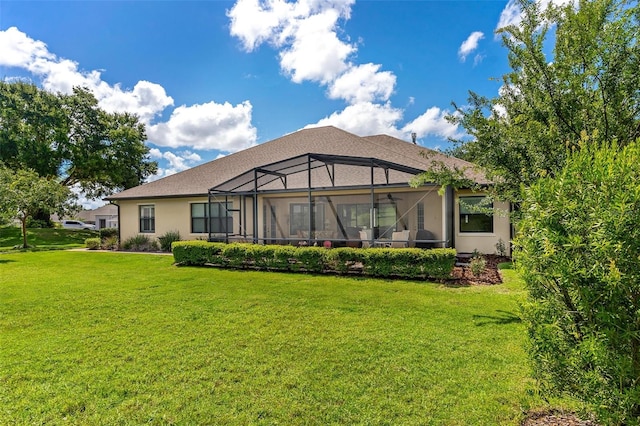 rear view of house featuring glass enclosure, stucco siding, and a yard