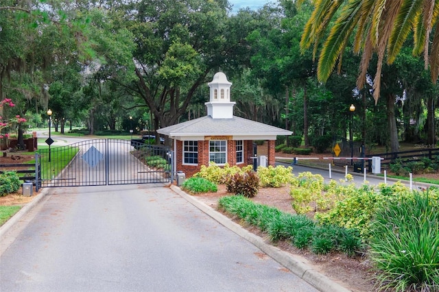 view of road with a gate, curbs, a gated entry, and street lights