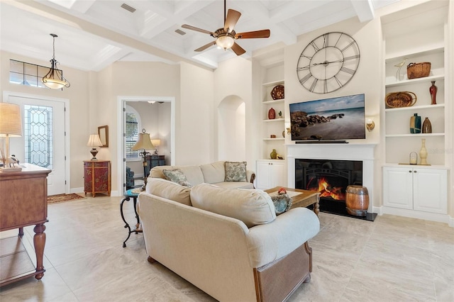 living room featuring baseboards, coffered ceiling, beamed ceiling, a lit fireplace, and built in shelves