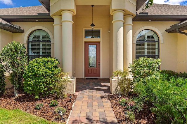 entrance to property featuring a shingled roof and stucco siding