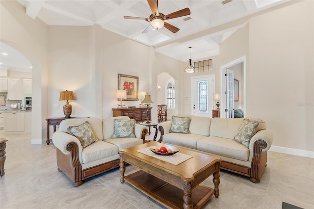 living area featuring arched walkways, coffered ceiling, a towering ceiling, and baseboards