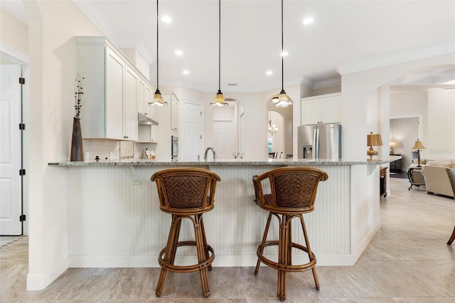 kitchen featuring a breakfast bar, arched walkways, backsplash, light stone countertops, and stainless steel fridge