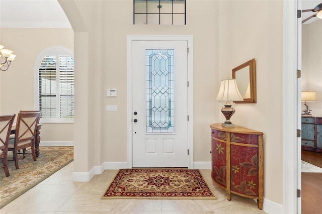 foyer with arched walkways, ceiling fan with notable chandelier, tile patterned flooring, and baseboards