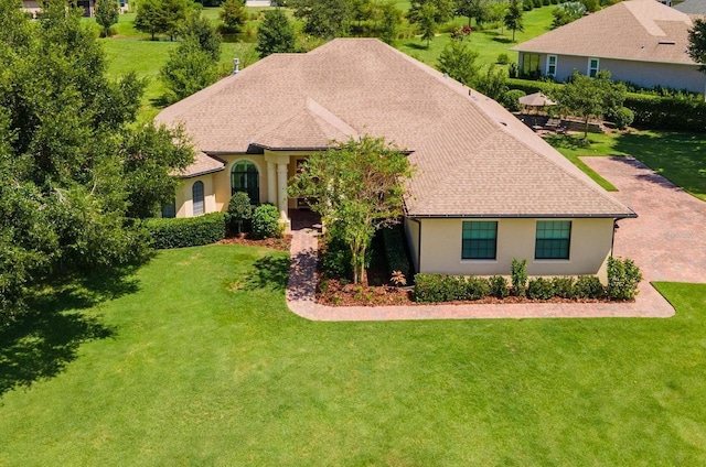 view of front facade featuring a front lawn, roof with shingles, and stucco siding