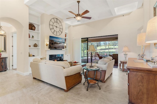 living area with built in features, beam ceiling, a glass covered fireplace, coffered ceiling, and baseboards