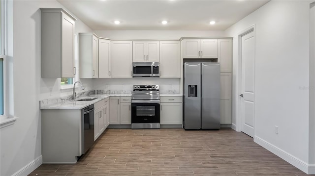 kitchen with light stone counters, stainless steel appliances, light wood-type flooring, sink, and white cabinets