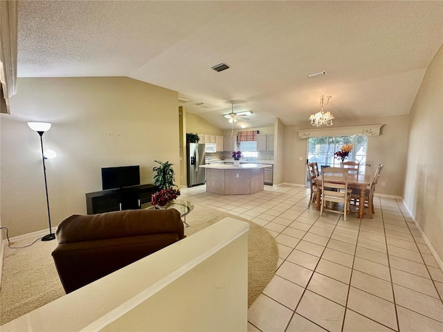 living room with light tile patterned floors, visible vents, vaulted ceiling, a textured ceiling, and ceiling fan with notable chandelier