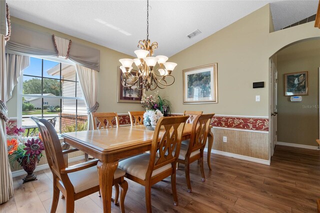 dining room featuring a textured ceiling, vaulted ceiling, a notable chandelier, and hardwood / wood-style flooring