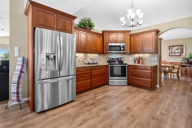 kitchen with tasteful backsplash, light hardwood / wood-style flooring, light stone counters, an inviting chandelier, and appliances with stainless steel finishes