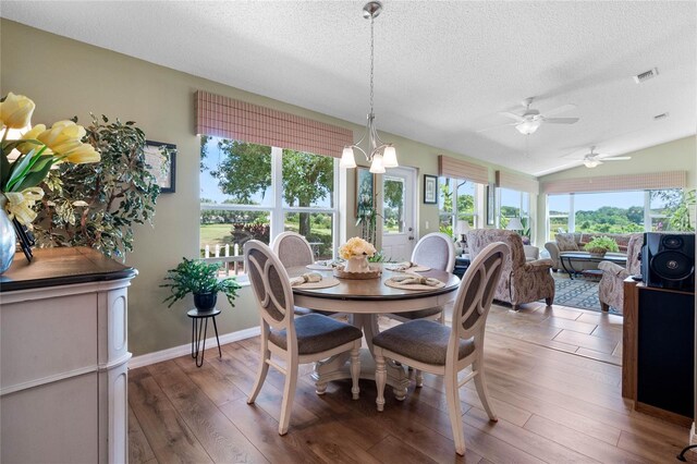 dining space with ceiling fan with notable chandelier, dark hardwood / wood-style floors, a textured ceiling, and vaulted ceiling